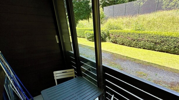 A balcony with a table and chairs, overlooking a well-maintained garden and a fence. - Le Pradet A 781 - Mont Dore 4 Pers (Mont-Dore)
