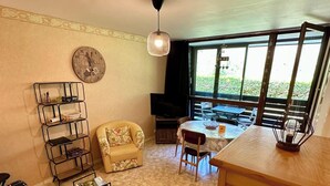 A cozy living area with a round table, a sofa, a small armchair, and a bookshelf. - Le Pradet A 781 - Mont Dore 4 Pers (Mont-Dore)