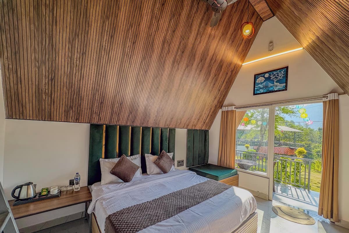 A bedroom with a sloped ceiling, a bed with a headboard, a nightstand, a window with a view, and a balcony.