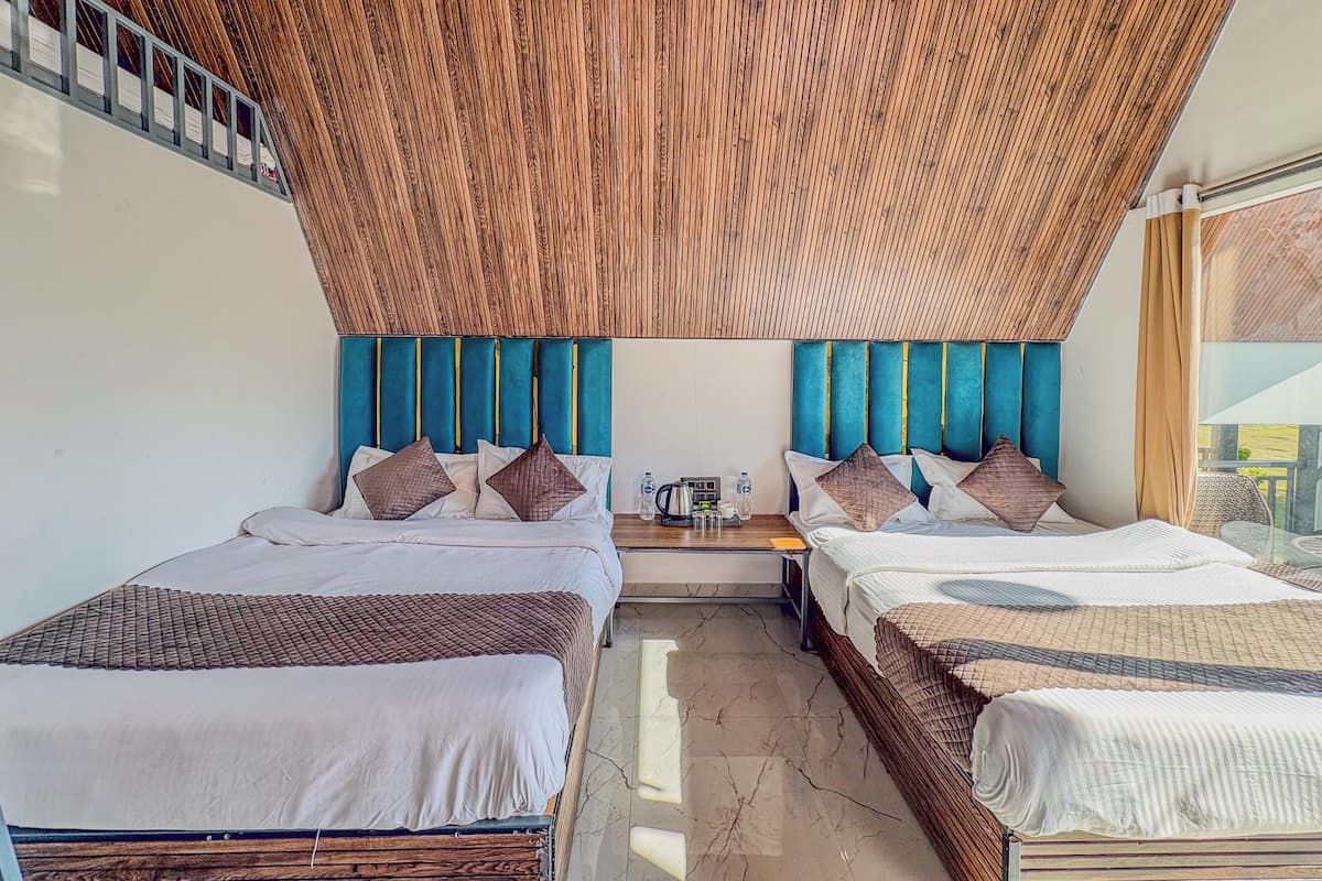 A hotel room with two beds, a wooden ceiling, and a view through a window.