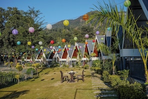 A courtyard with a lawn, a table with chairs, and colorful paper lanterns. - The Jungle Walker Resort  (Rishikesh)