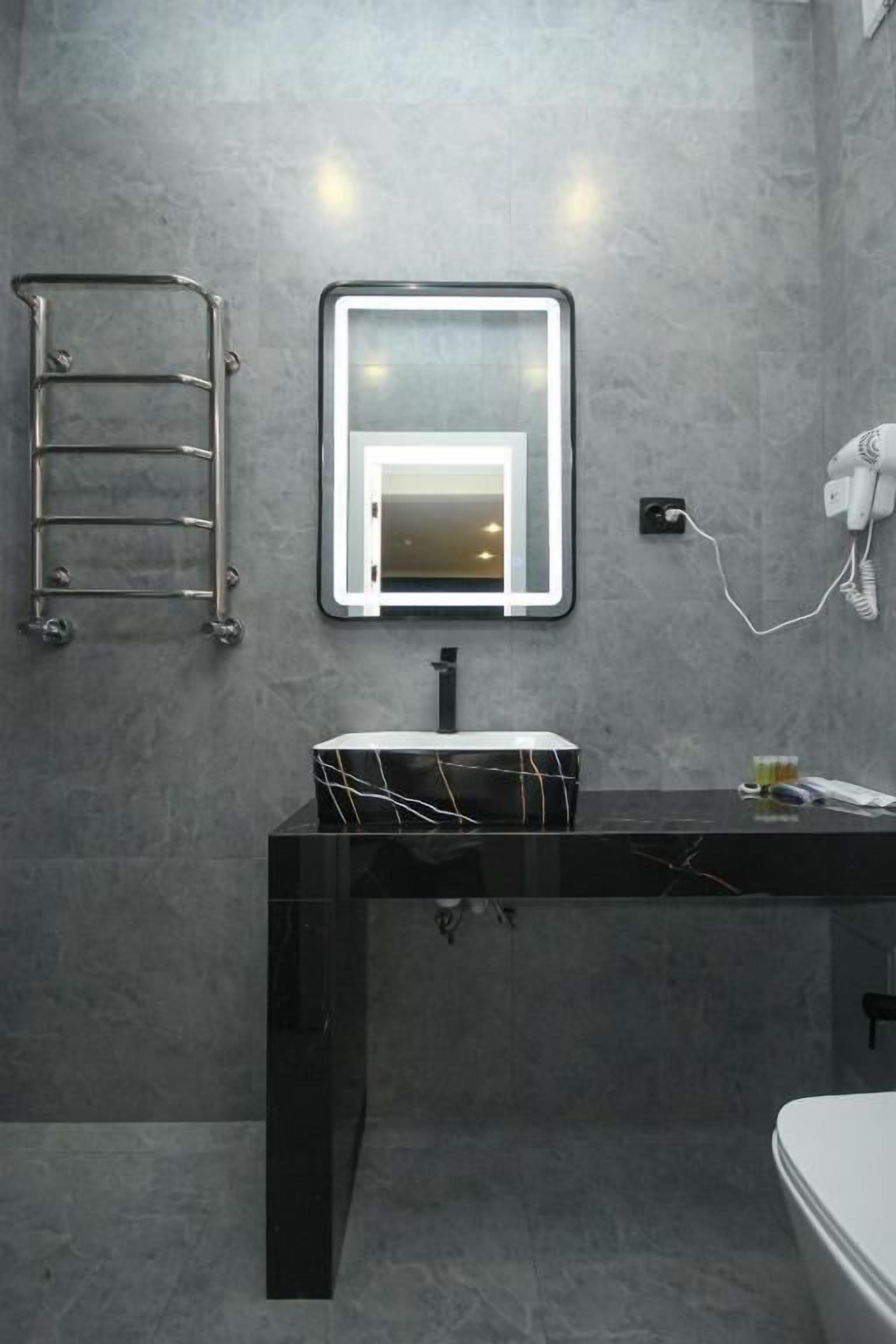 A modern bathroom with a black marble sink, a towel rack, a mirror with integrated lighting, and a hairdryer on the wall.