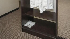 Un dressing où sont suspendues deux robes blanches sur un portant et une paire de chaussons posée sur une étagère.