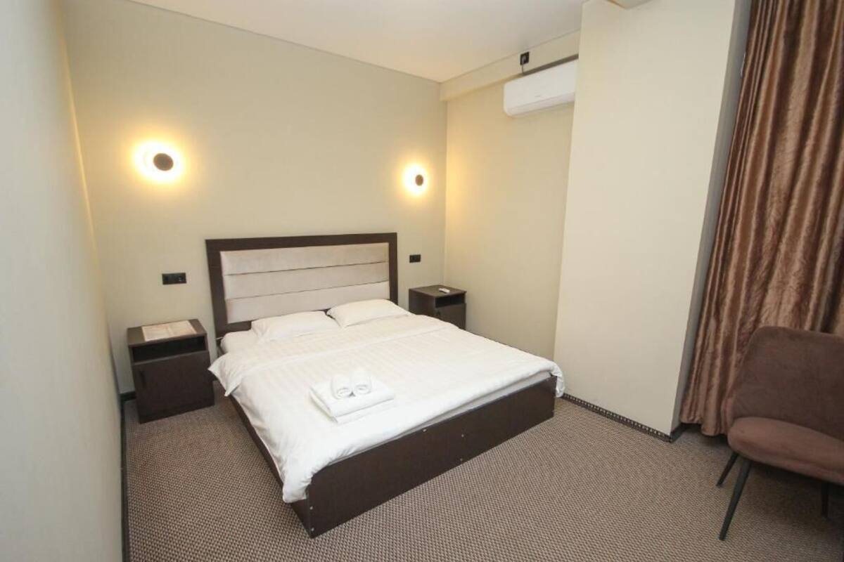 Una habitación de hotel con una cama, mesitas de noche, una silla y una cortina.