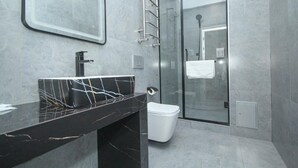 Une salle de bain moderne avec un lavabo en marbre noir, une douche en verre et des toilettes blanches.