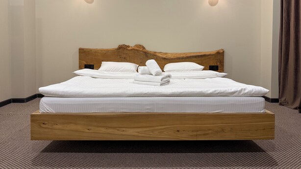 Un lit bien fait, avec du linge de lit et des serviettes blancs, une tête de lit en bois et deux appliques murales.