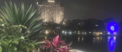 Una vista nocturna de un hotel con un cuerpo de agua al frente y un edificio con la iluminación 'Sheraton' en el fondo.