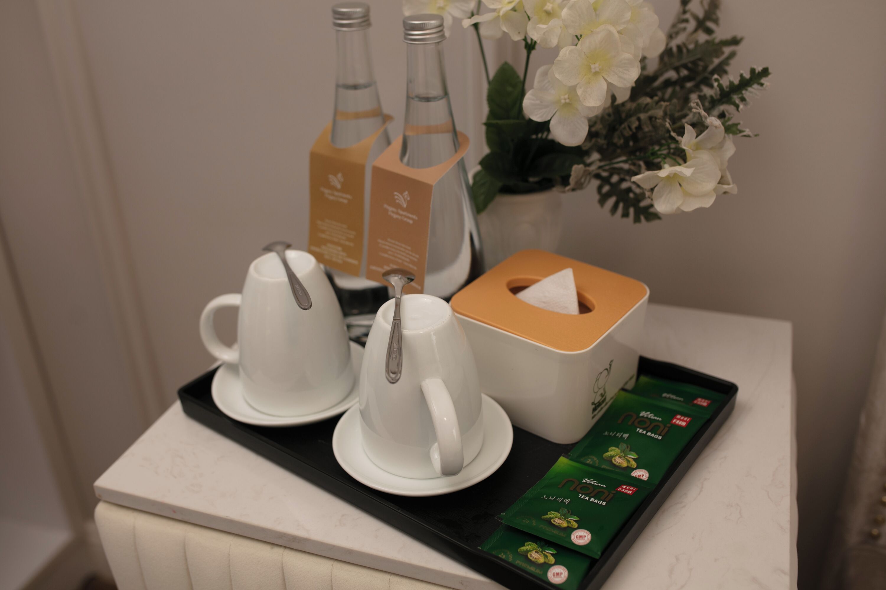 A tray with tea bags, a tissue box, and two white teapots on a white table.