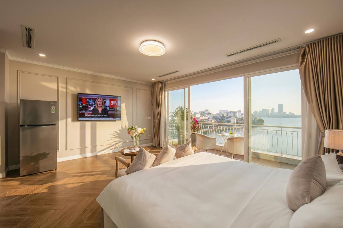 Una habitación de hotel con una cama grande, un televisor en la pared, un balcón con vistas a la ciudad y un refrigerador.