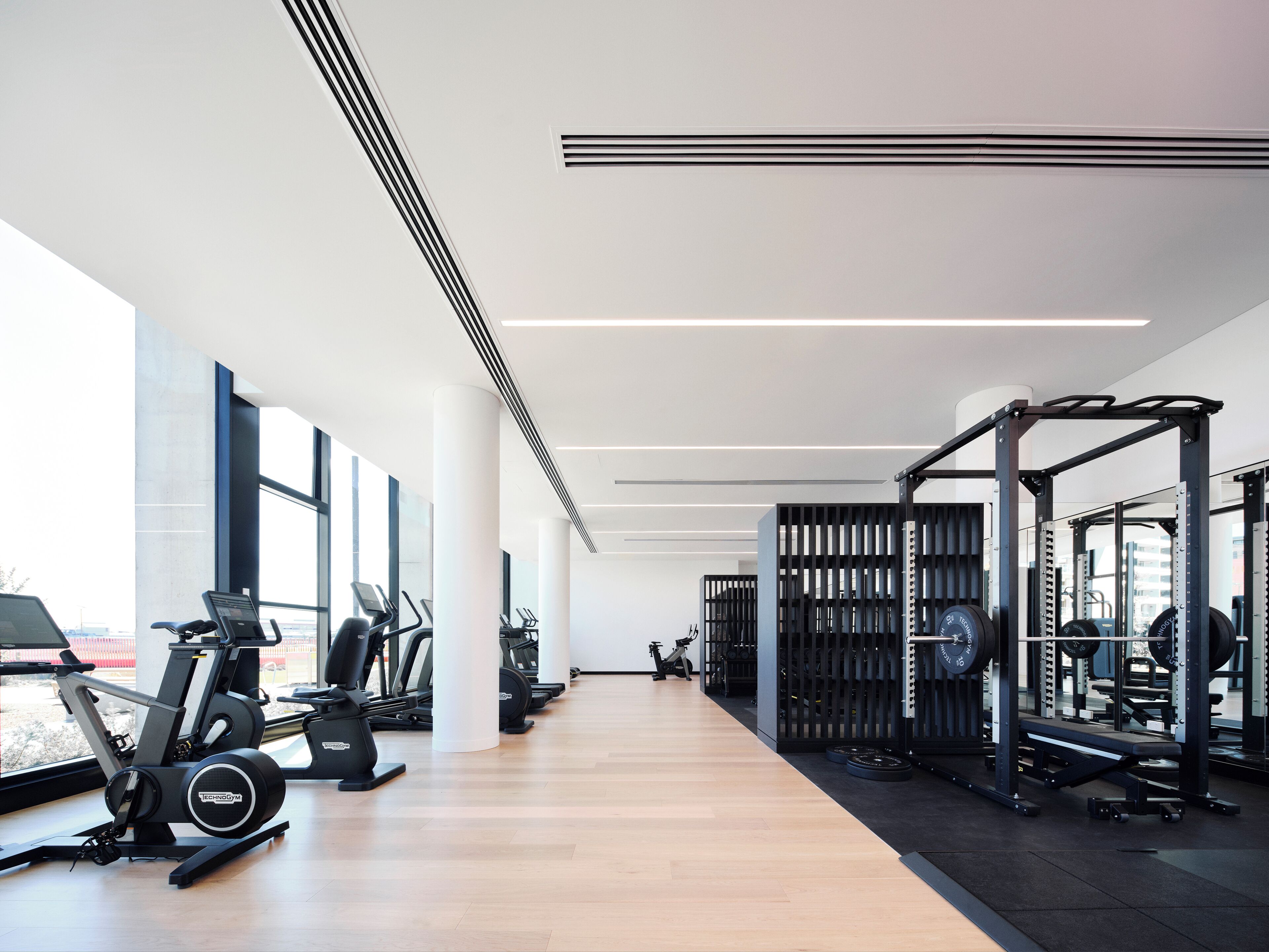 A modern gym with cardio machines, weightlifting equipment, and large windows offering views of the outside.