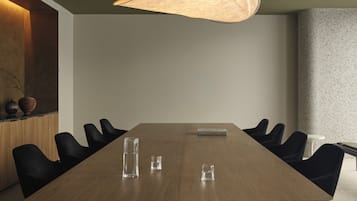 A conference room with a long table, black chairs, a hanging light fixture, and a vase on the sideboard.