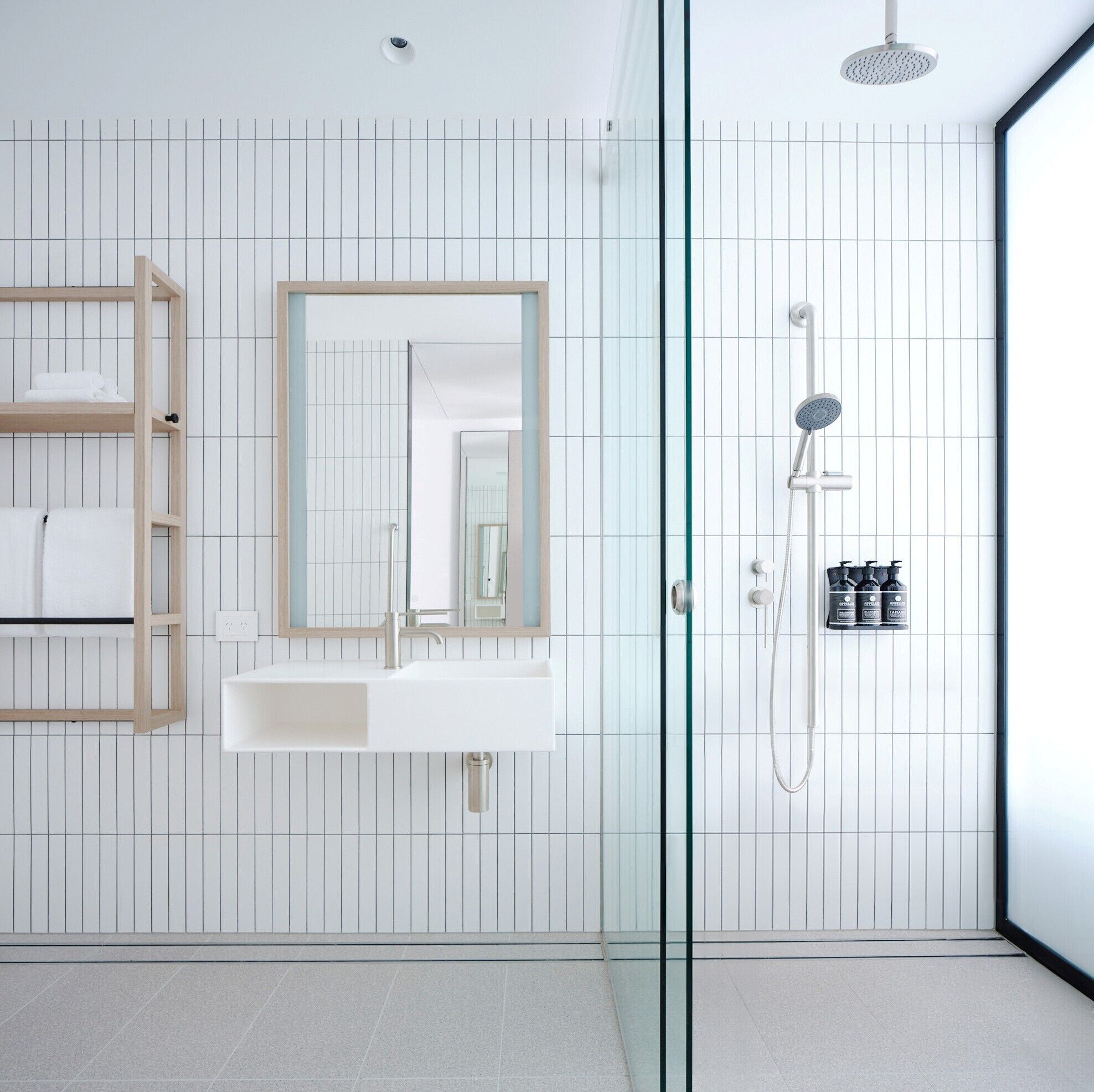 Un baño moderno con cabina de ducha de vidrio, espejo con marco de madera y lavabo blanco.