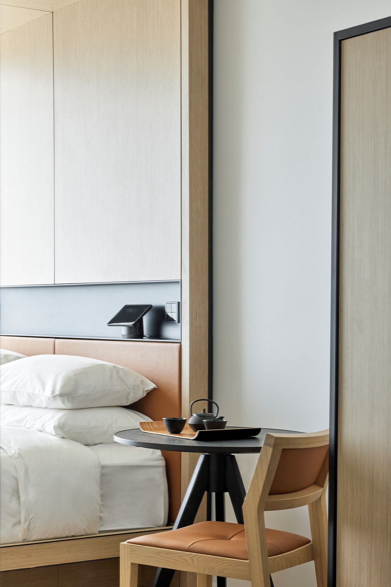 A hotel room with a bed, a small table with a tea set, a chair, and a wardrobe.