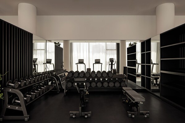 Une salle de sport équipée de supports à poids, d’haltères, de bancs et d’appareils d’exercice.