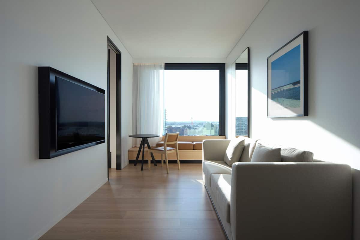 A modern living room with a flat-screen TV, a sofa, a dining table, and a large window with a city view.
