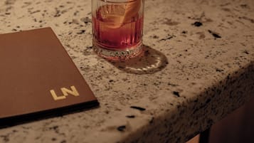 A glass of amber-colored drink on a speckled countertop, a brown notebook with 'LN' on it, and a chair.