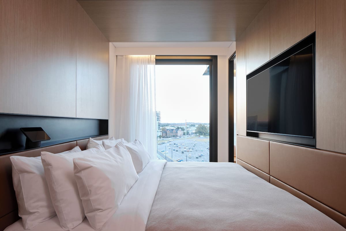 A modern hotel room with a large bed, a flat-screen TV, and a city view.