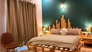 A modern bedroom with a bed, wooden headboard, two bedside tables with lamps, a chair, and a black rug. - Motwani Stays By Dr Richa Motwani (Jaipur)