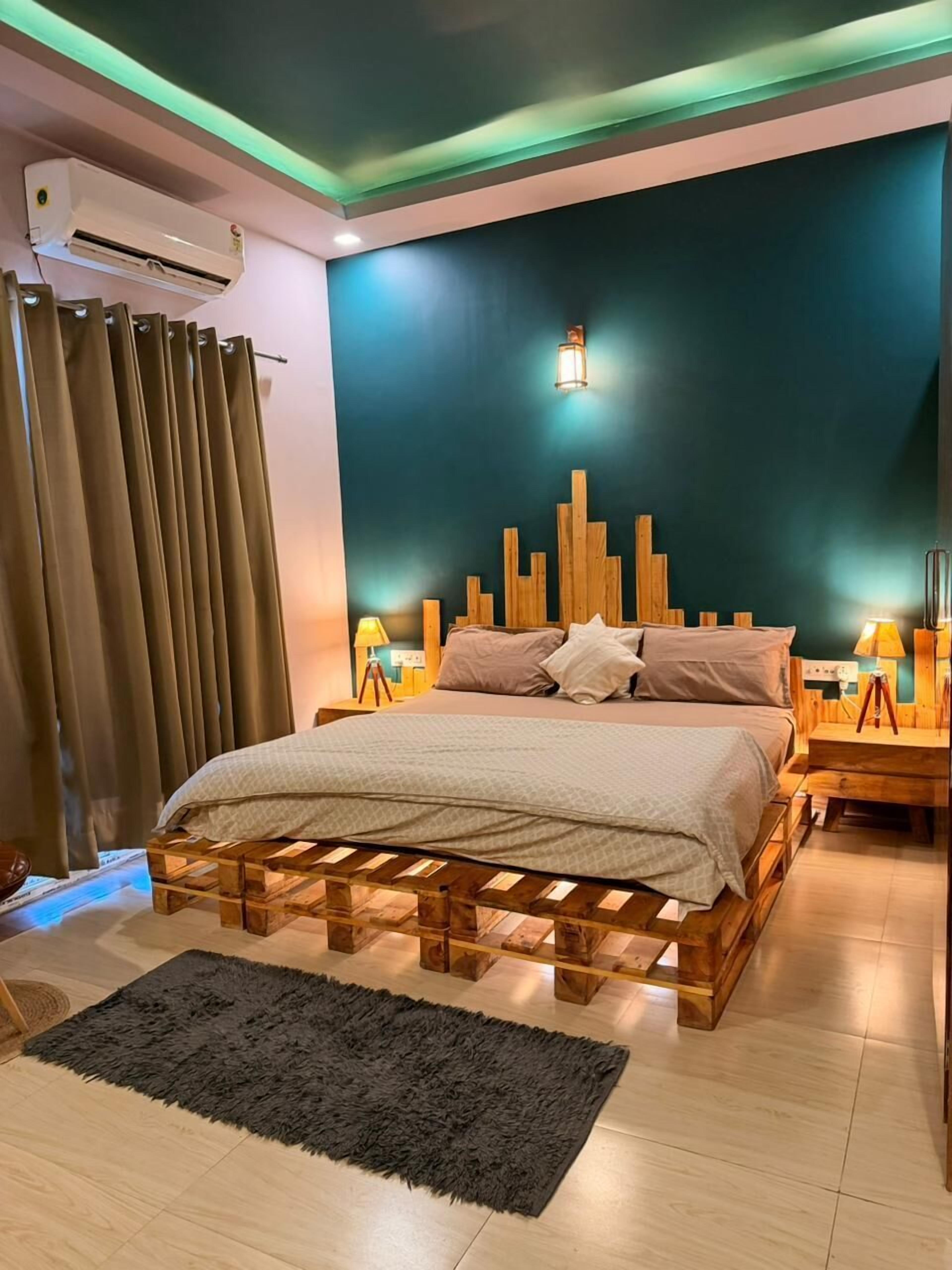 Een slaapkamer met een bed op een houten pallet, een zwart vloerkleed en een luchtverkoeler aan de muur.