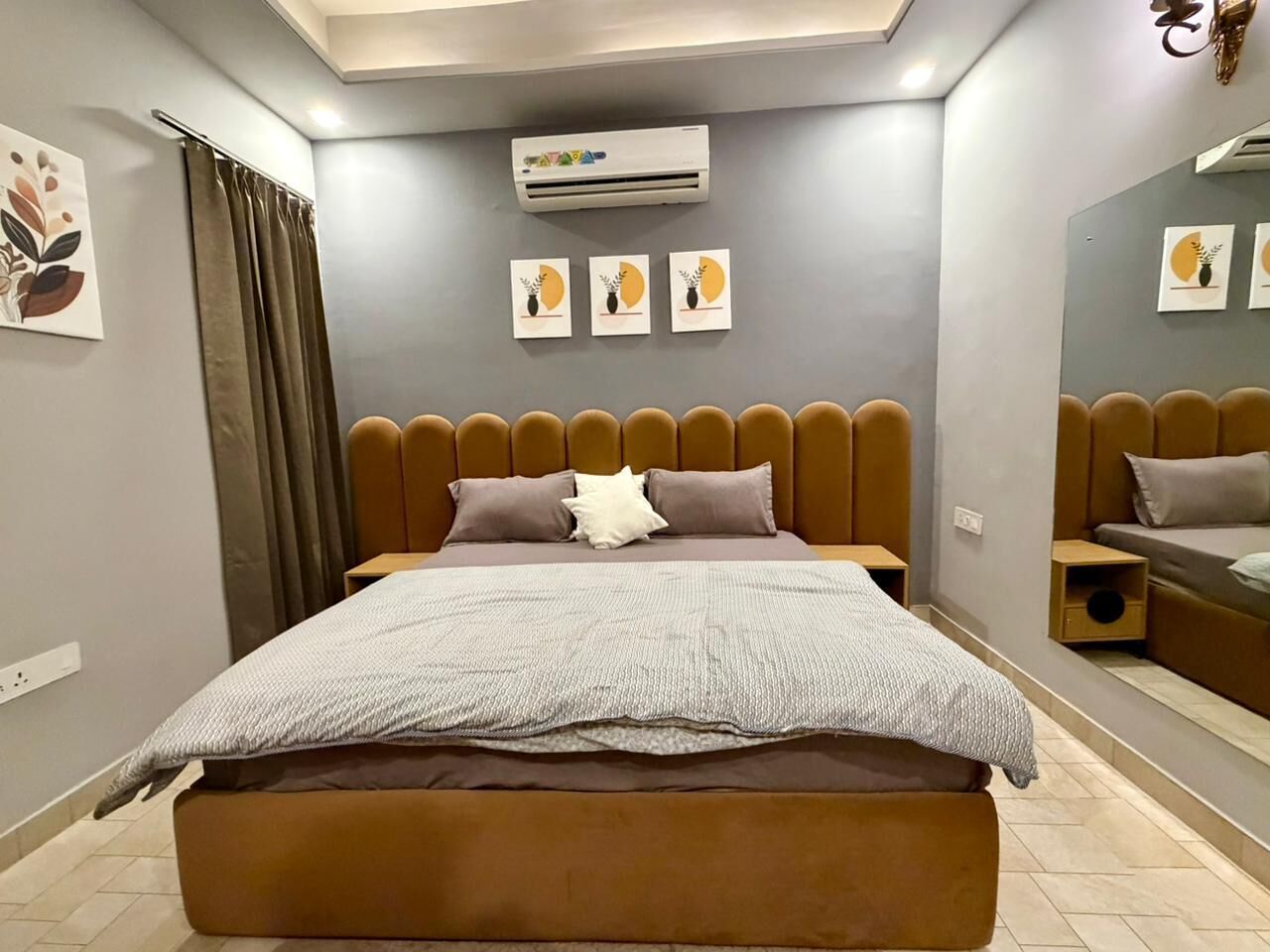 Een moderne slaapkamer met een groot bed, een hoofdeinde, een nachtkastje, een spiegel en een airconditioner.