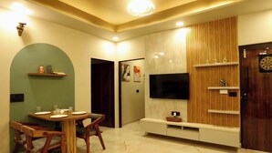 A modern living room with a dining area, a flat-screen TV, and a wooden entertainment unit. - Motwani Stays By Dr Richa Motwani (Jaipur)