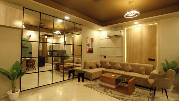 A modern living room with a sectional sofa, a coffee table, and a large mirror. - Motwani Stays By Dr Richa Motwani (Jaipur)