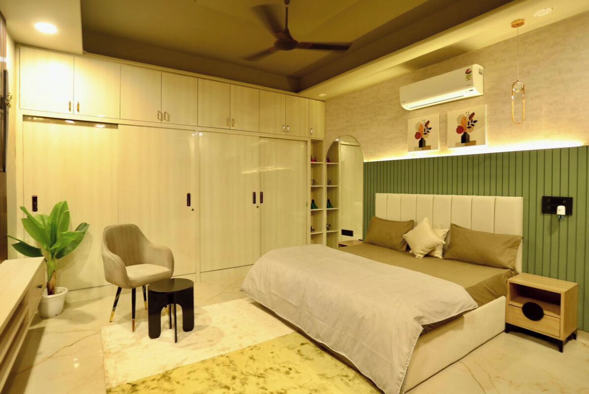 A bedroom with a bed, a chair, a small table, a nightstand, and a wardrobe.