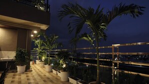 A rooftop terrace with potted plants, a checkered floor, and a view of the city at night. - Motwani Stays By Dr Richa Motwani (Jaipur)