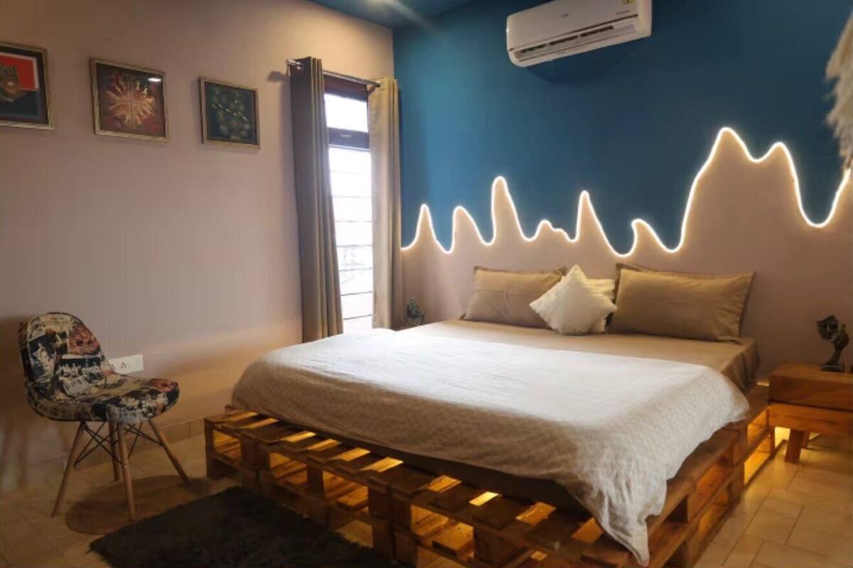 Ein Schlafzimmer mit einem Bett auf einem Holzboden, einem Sessel, einem Nachttisch und einer Wand-Klimaanlage.