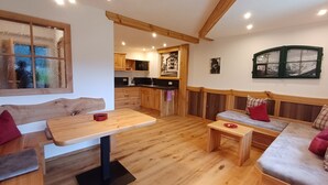 A cozy interior with a wooden dining table, a sofa, and a bench. There is a kitchen area with wooden cabinets and a window with a view. - Grünstein - 2-room apartment, south and east-facing balcony, 2 persons, 40 sqm, safe, kitchenette (Ramsau bei Berchtesgaden)