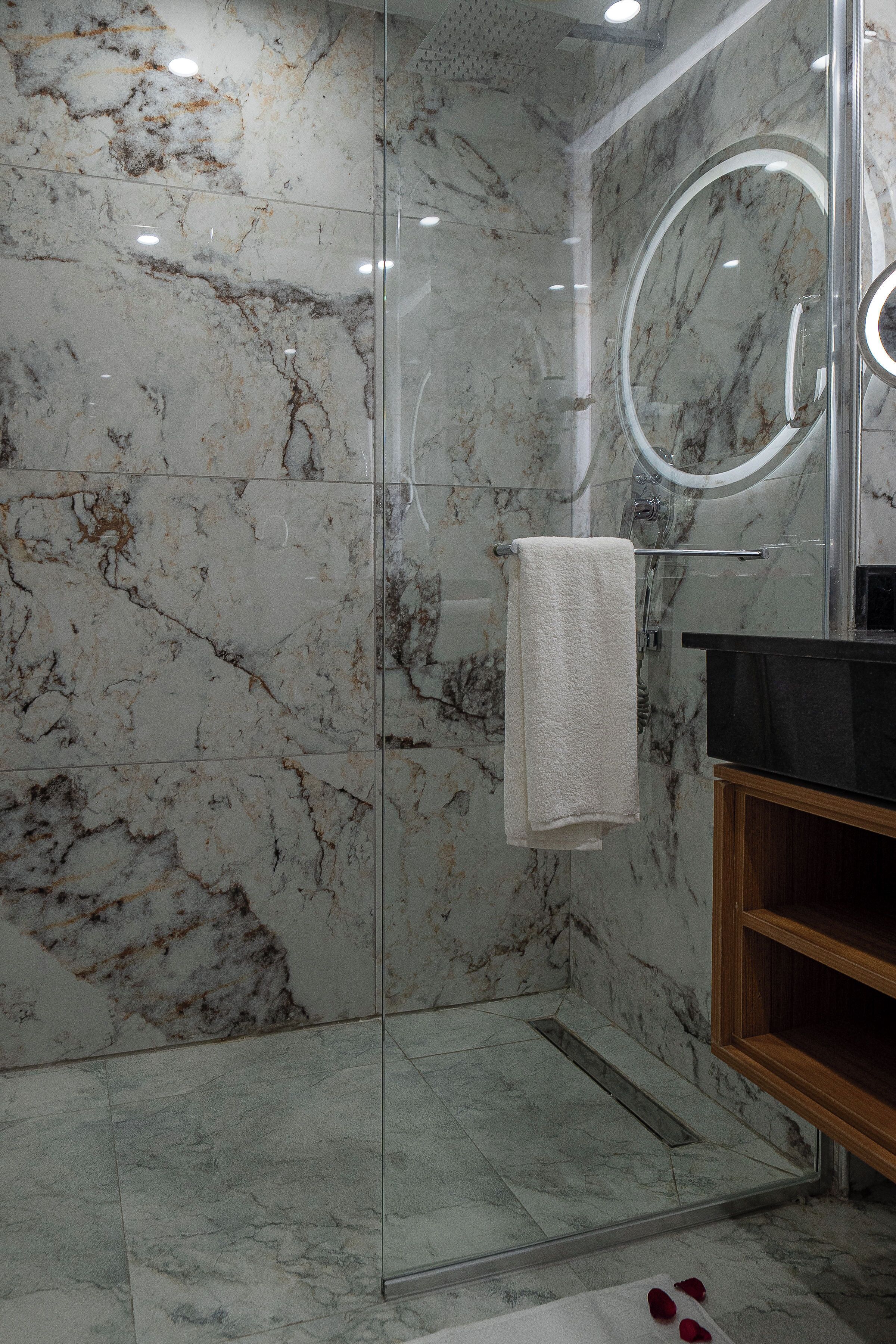 Un baño moderno con cabina de ducha de vidrio, paredes de mármol y tocador de madera.