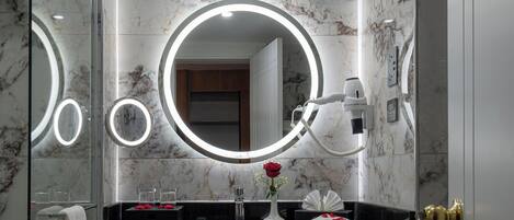 A bathroom with a marble wall, a sink with a mirror, and a towel rack.