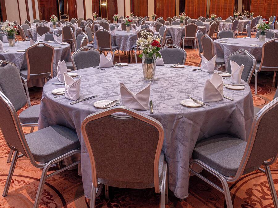 A banquet hall with round tables, grey chairs, and floral centerpieces.