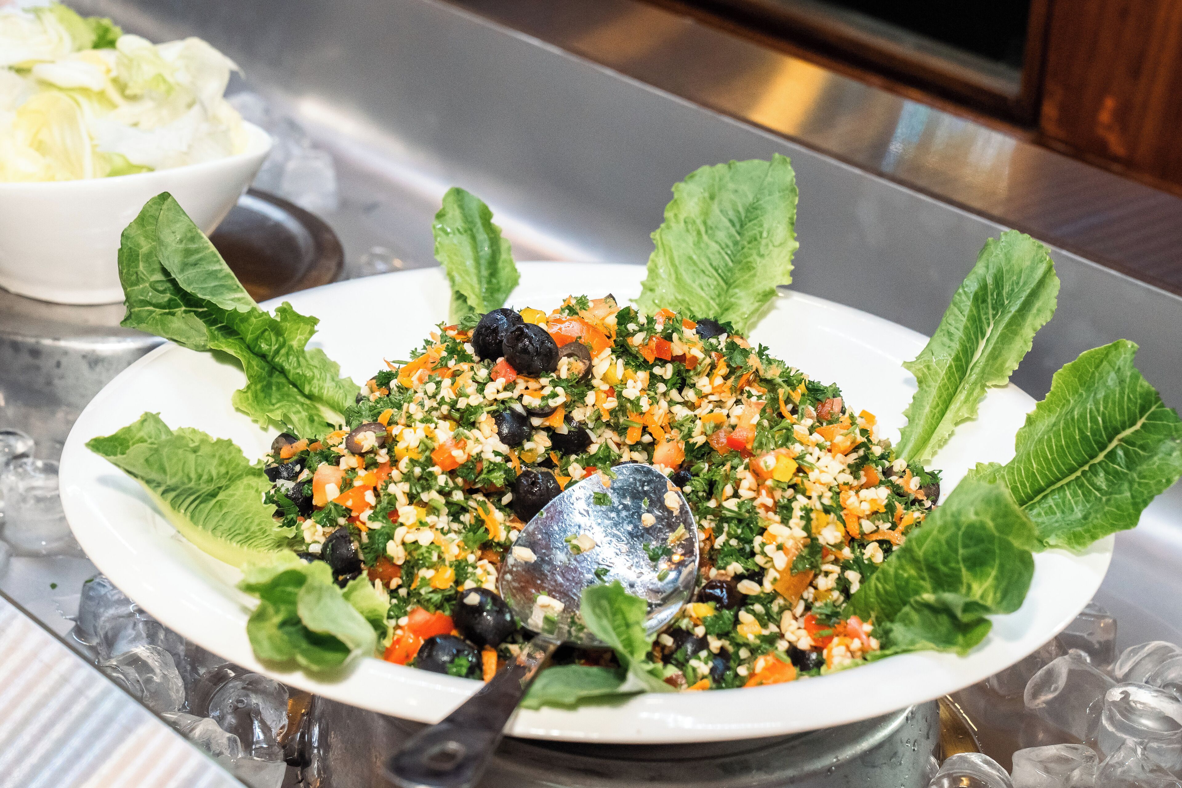 A plate of salad with various vegetables and olives, garnished with lettuce leaves.