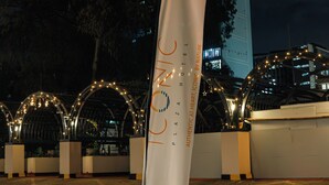A flag with "ICONIC HOTEL" text, a paved area with a circular design, and a building with illuminated windows in the background. - Iconic Plaza Hotel (Nairobi)