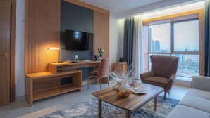 A modern living room with a TV mounted on a wooden panel wall, a coffee table with a vase, a sofa, and a chair. - Iconic Plaza Hotel (Nairobi)