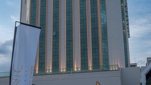 A modern hotel building with a prominent vertical glass facade and a landscaped entrance area with a water feature. - Iconic Plaza Hotel (Nairobi)
