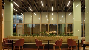 A modern interior with a green sofa, wooden tables, and chairs, large windows, and a ceiling with linear lighting. - Iconic Plaza Hotel (Nairobi)