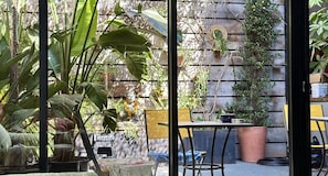 Une terrasse avec une table et des chaises, entourée de plantes en pot et d’une statue de Bouddha.