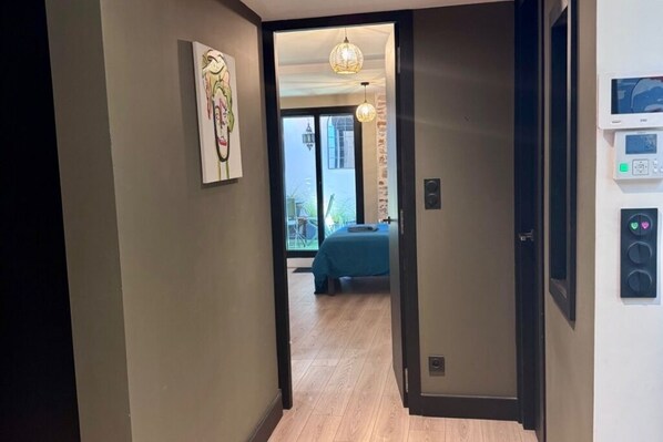 Un couloir menant à une chambre à coucher, où se trouvent un lit, un tableau accroché au mur et un thermostat également fixé au mur.