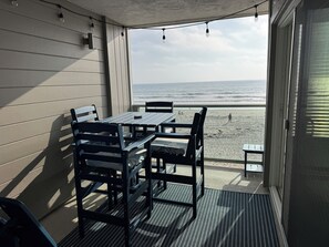 A covered patio with a table and chairs, overlooking a beach. - Beachfront Top Floor Condo Private Deck (San Diego)