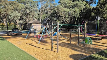 A playground with various play structures, a fenced area, and a small building.