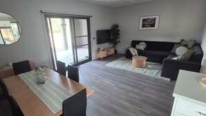 A modern living room with a dining area, a large mirror, a flat-screen TV, a sofa, and a coffee table. - Family Luxury Country Retreat Pool & Spa – Lodge 2 (Yarrambat)