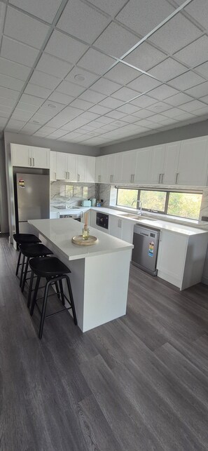 A modern kitchen with white cabinets, a large island with bar stools, a stainless steel refrigerator, and a dishwasher.