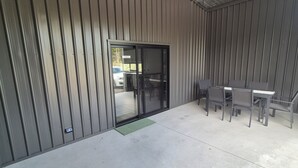 A covered outdoor area with a sliding glass door leading to a parking lot. There is a table and chairs set up for outdoor dining. - Family Luxury Country Retreat Pool & Spa – Lodge 2 (Yarrambat)