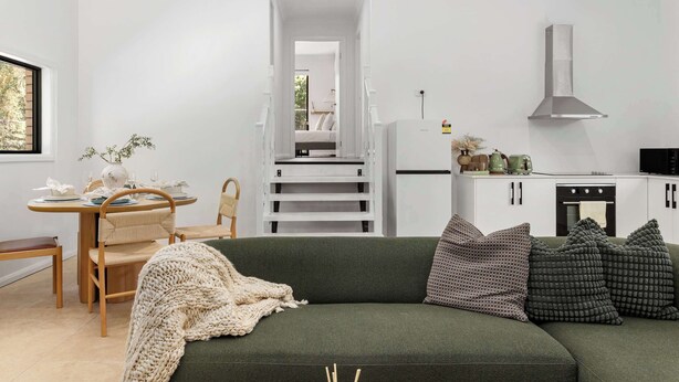 A modern living room with a green sofa, wooden dining table, and white cabinets. - New 2BR GrannyFlat,Near Movie World, Wet'Wild,Pool (Helensvale)