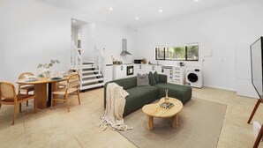 A modern living room with a dining area, a green sofa, a coffee table, and a kitchen in the background. - New 2BR GrannyFlat,Near Movie World, Wet'Wild,Pool (Helensvale)