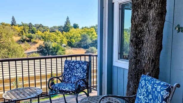 A wooden deck with two patterned chairs and a small table, overlooking a scenic landscape. - Entire home in Folsom, California (Folsom)