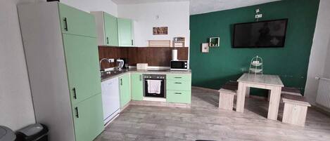 Un espace de vie compact comprenant un coin cuisine, un coin repas et un téléviseur fixé sur un mur vert.