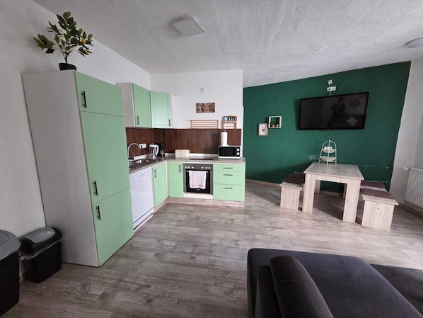 A compact living space with a kitchenette, a dining area, and a TV mounted on a green wall.